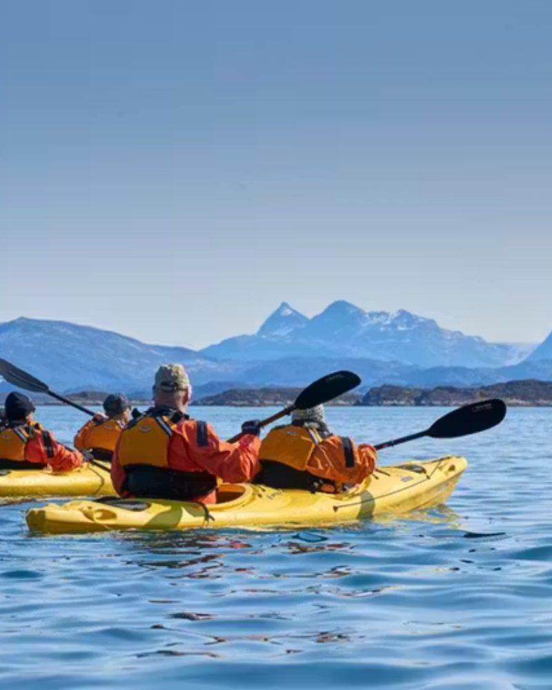 Guests paddling yellow kayaks below distant mountains