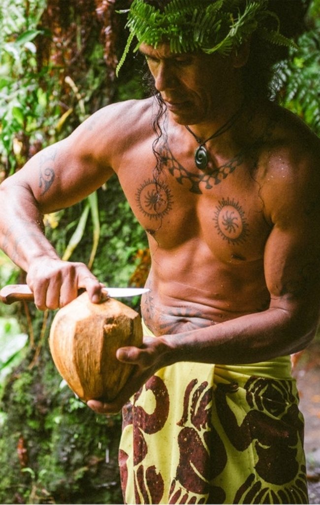 A Polynesian man in a pareo carving a coconut shell