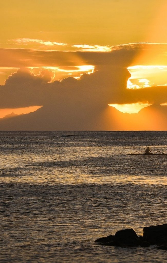 An outrigger canoe on the water at sunset in the Society Islands