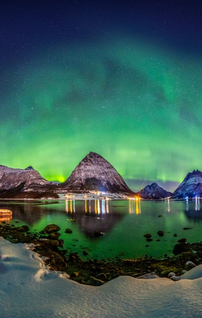 Green northern lights over snowy peaks and a fjord at night