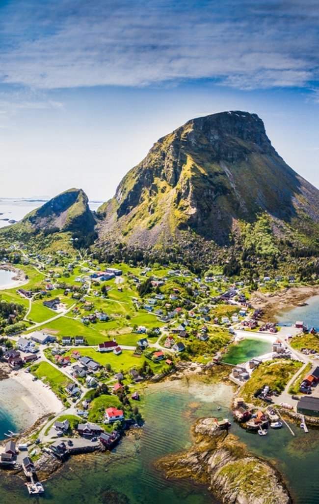 Aerial view of a green island village below a steep peak on the Norwegian coast