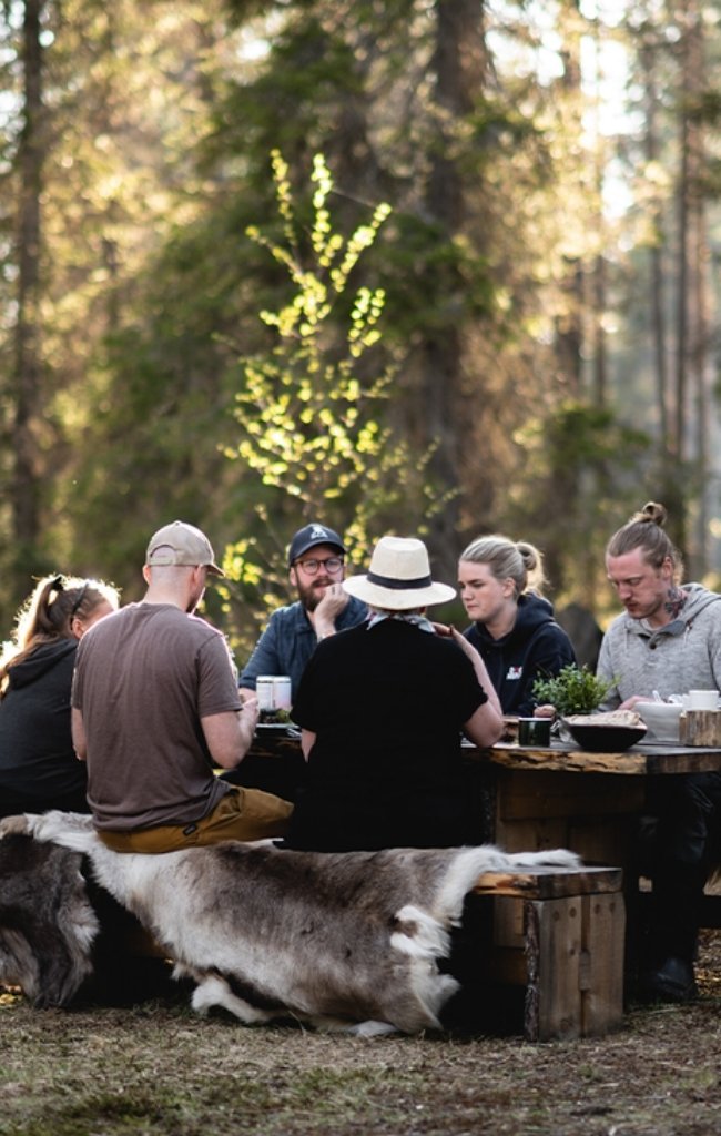 Travelers sharing a meal at a wooden table in a Swedish forest