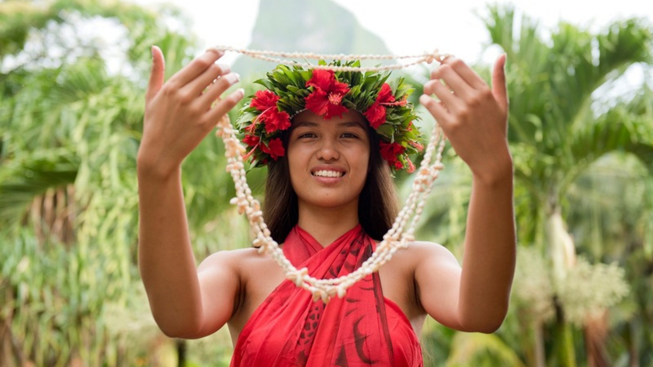 A Tahitian woman in a flower crown offering a shell necklace
