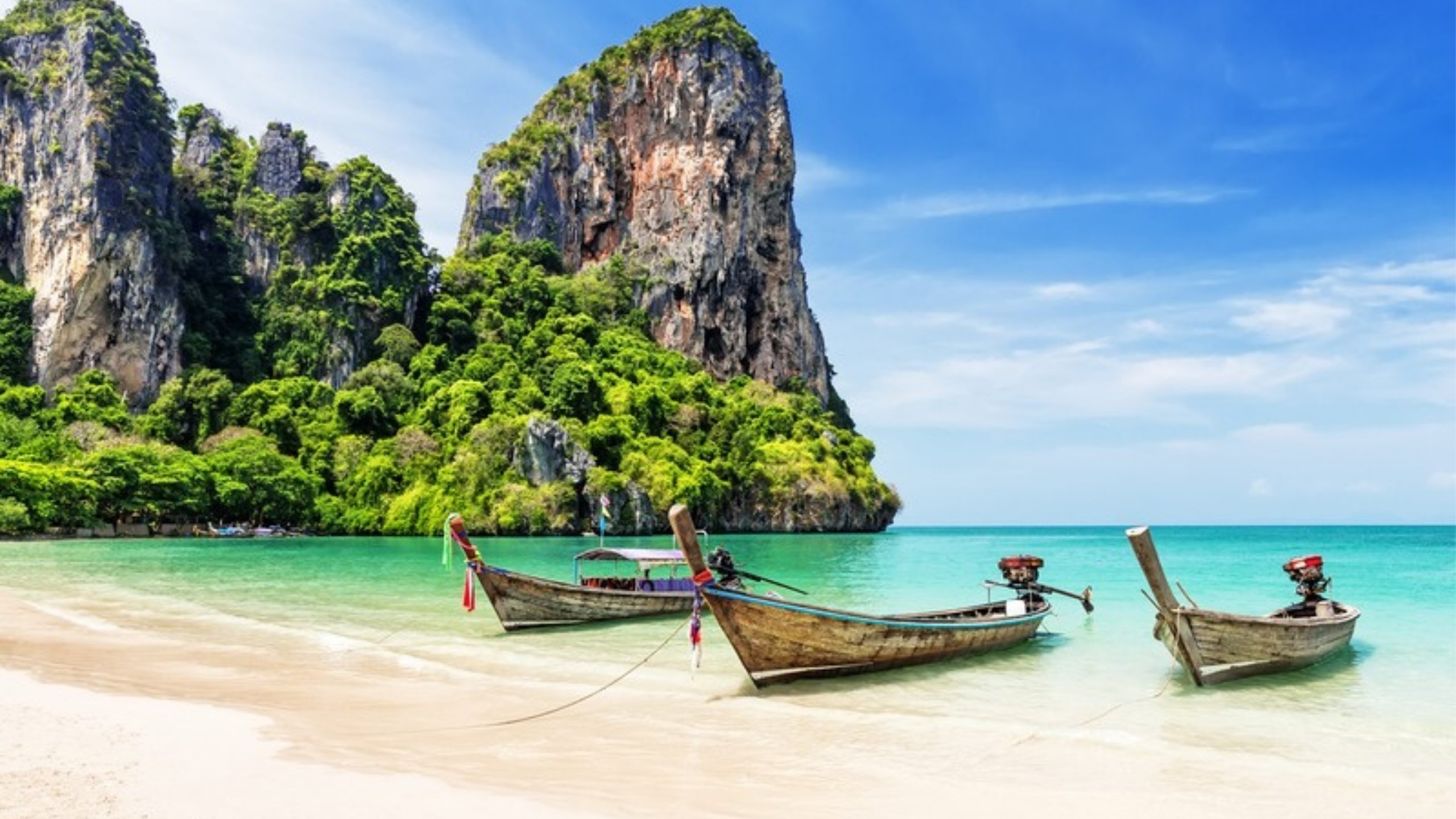 Longtail boats in a turquoise bay below limestone cliffs in Krabi