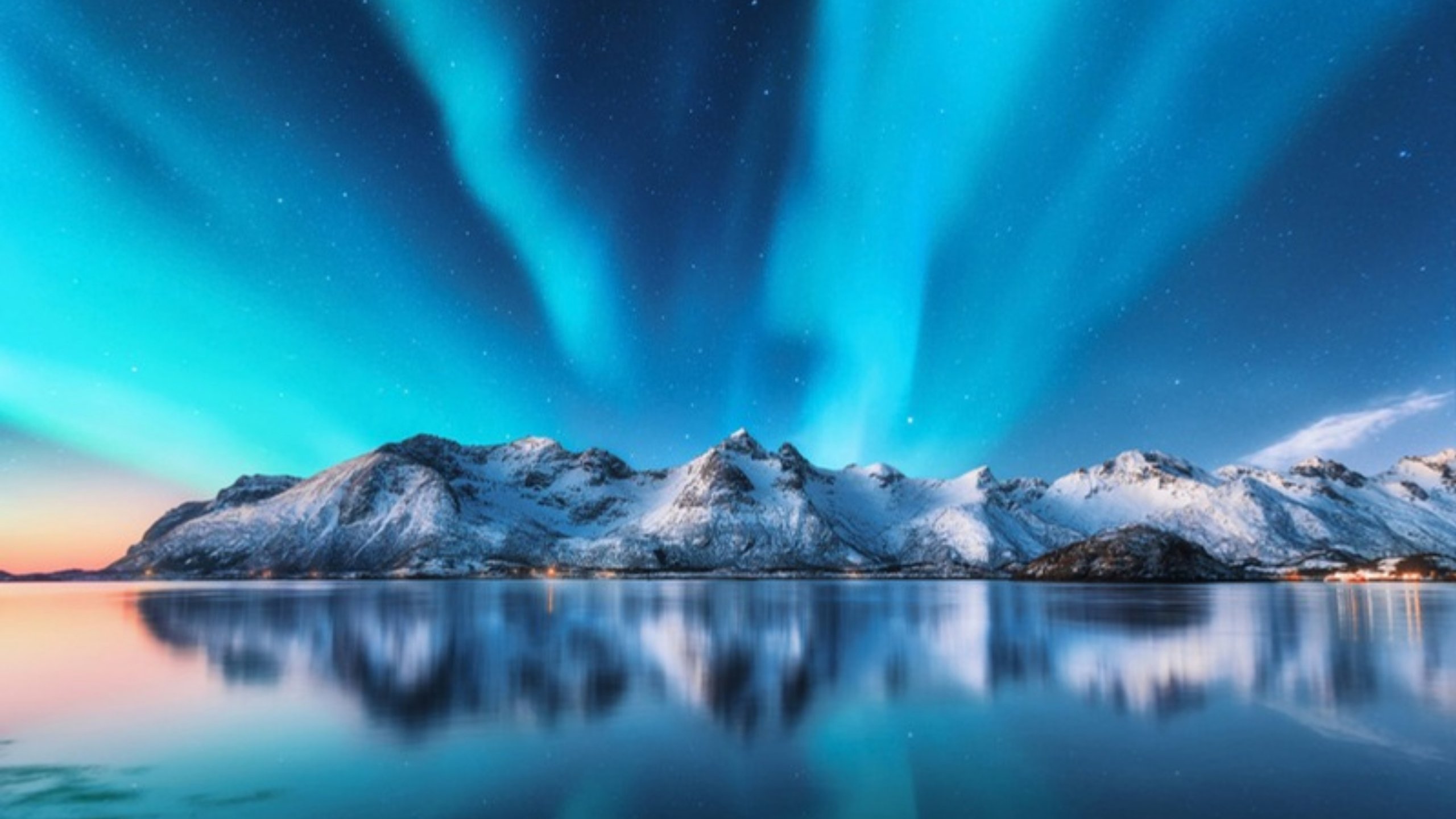 Northern lights over snow-covered mountains reflected in a calm fjord