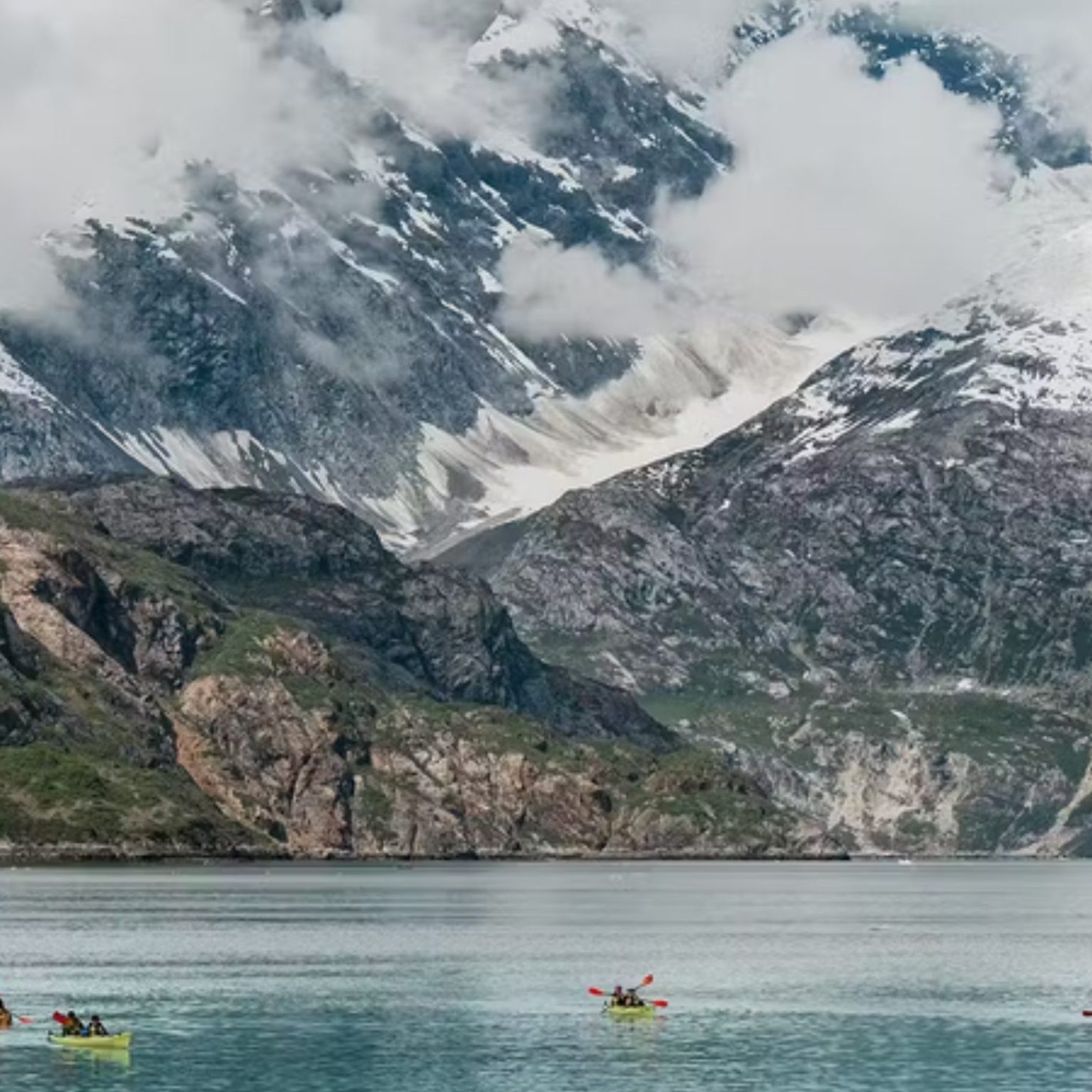 Kayakers paddling below snowy mountains in Alaska