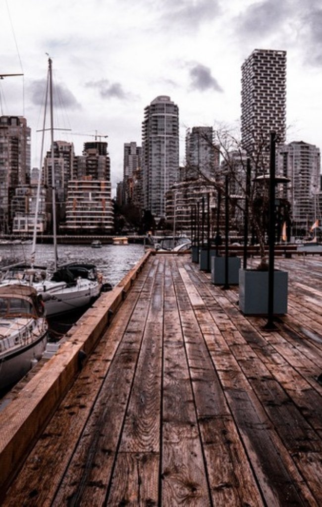 A wooden dock and sailboats below the downtown towers of Vancouver
