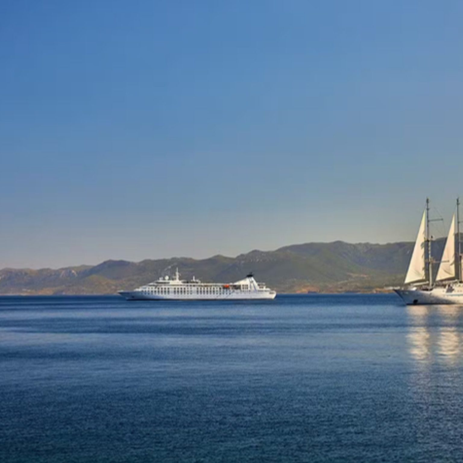 A Windstar sailing yacht and motor yacht in a calm Greek bay